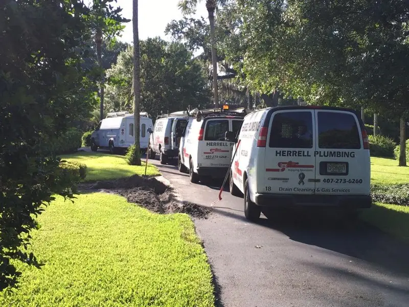 Four Herrell Plumbing service vans lined up along a residential driveway at a job site
