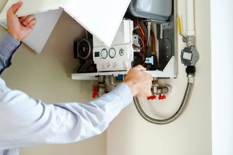 Technician servicing the valves inside an opened wall-mounted tankless water heater