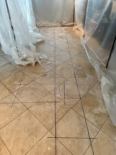 Beige tile floor with dark straight saw lines marked across it and clear plastic sheeting hanging on either side of the room