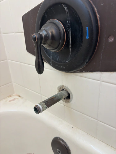 Old oil rubbed bronze tub and shower trim on a rectangular cover plate above a corroded spout nipple sticking out of white tile