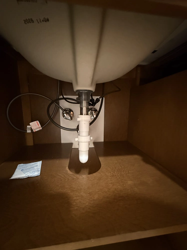 Under cabinet view of a new white PVC tailpiece and P trap below a sink, with disposal wiring run to one side