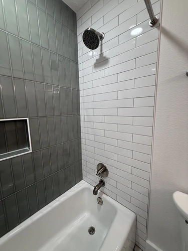 Brushed nickel shower head on white subway tile beside a vertical green grey tile accent wall with a recessed niche