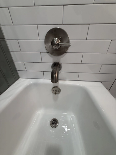 Brushed nickel single handle tub and shower valve with a round escutcheon and matching spout on white subway tile above a white tub