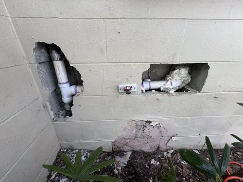 After the repair: two openings in a block wall, one showing a new white PVC tee joined to the cast iron stack, the other a new PVC waste arm sealed with foam