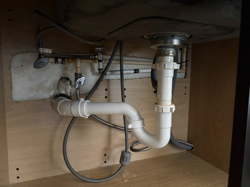 After the repair: a new white PVC P trap and trap arm under a stainless kitchen sink, running into the back wall of the cabinet