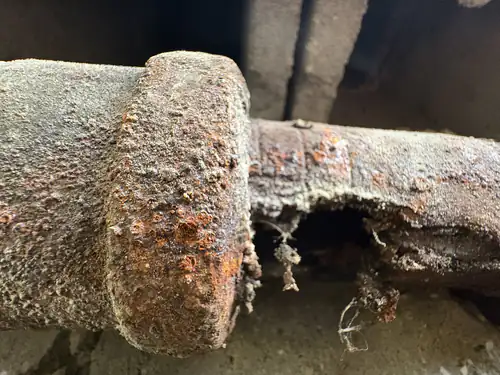 Before the repair: close up of a cast iron drain pipe beside its hub joint, with the underside rusted open into a ragged hole