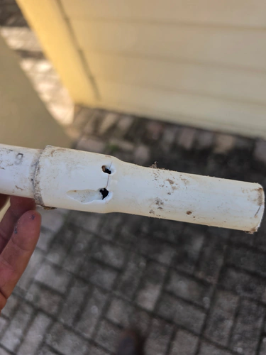 During the repair: a cut out length of white three quarter inch PVC pipe held in a hand, with two holes and a hairline crack beside the joint